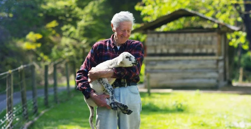 Danny carrying a lamb across the yard at the farm