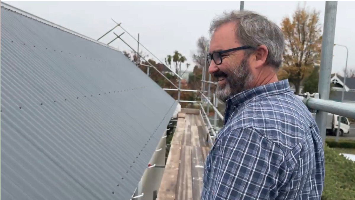 Johnnie smiling at the new corrugated roofline from the scaffold