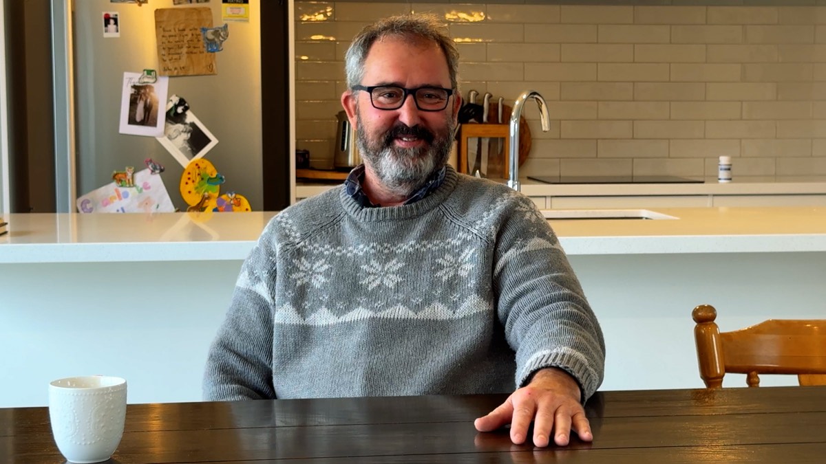 Johnnie sitting at his kitchen table in a grey jersey