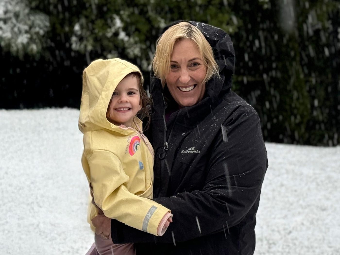 Jen holding her granddaughter in a yellow raincoat in a snowy garden